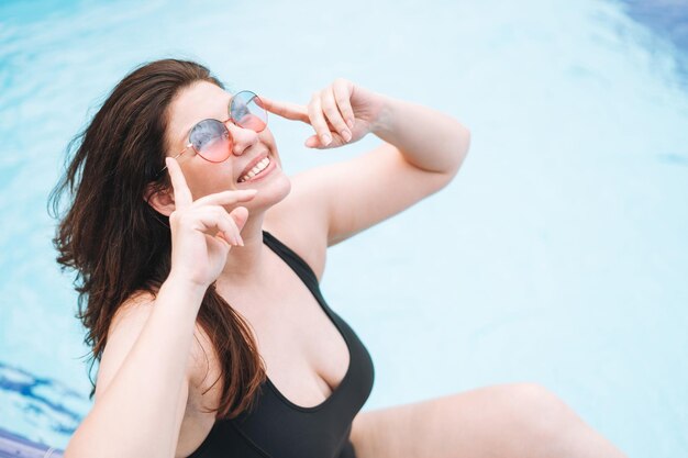 Stilvolle, glückliche junge Frau in schwarzem Badeanzug und Sonnenbrille in der Nähe des Hotelpools