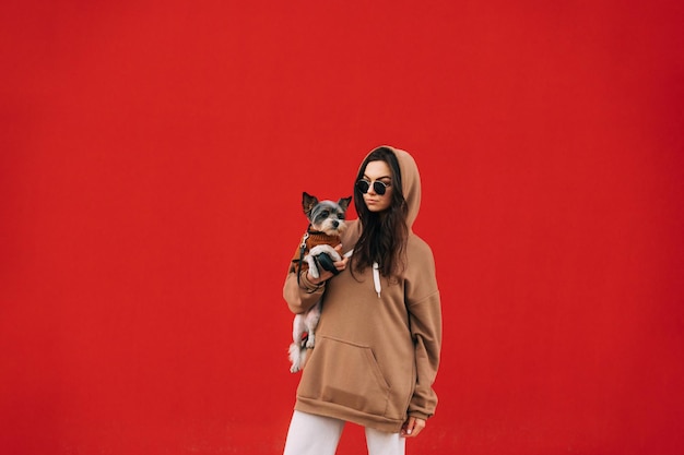 Stilvolle Hundebesitzerin mit Sonnenbrille und braunem Hoodie, die ihren kleinen Haustier-York-Terrier hält