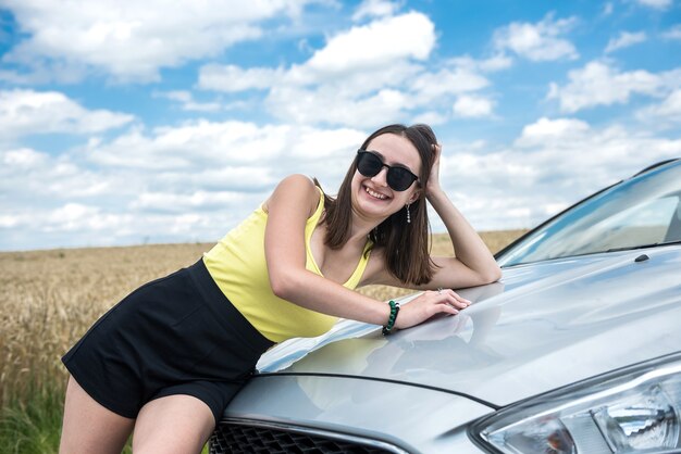 Stilvolle junge Frau macht eine Reisepause und ruht sich am Straßenrand in der Nähe des Autos aus