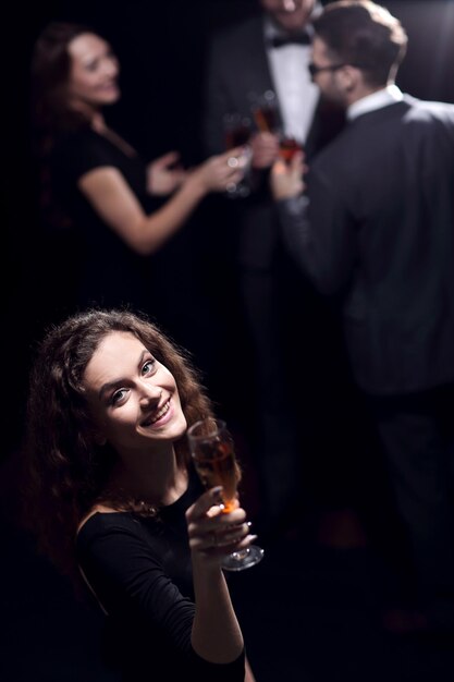 Stilvolle junge Frau mit einem Glas Champagner auf dem Hintergrund von Freunden