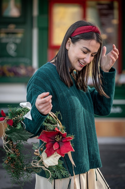 Stilvolle junge Frau mit einem Weihnachtskranz in roten und grünen Farben