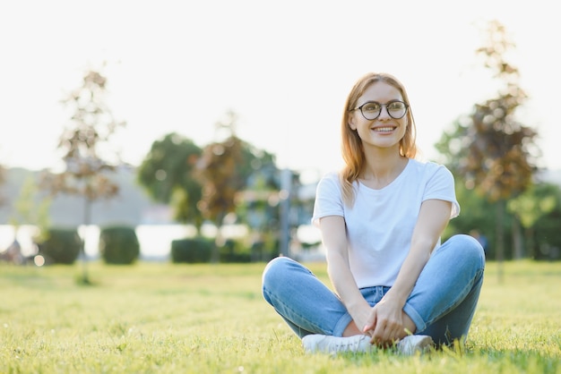 Stilvolle junge Frau verbringt Zeit im Park auf dem grünen Gras. Sommerferienkonzept.