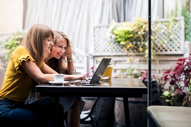 Stilvolle junge Frauen, die sich mit Kaffeetassen treffen, während sie den Laptop benutzen