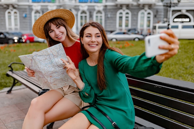 Stilvolle junge Frauen, die zusammen in Europa reisen, gekleidet in trendigen Frühlingskleidern und Accessoires mit Karte