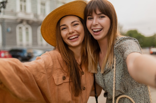 Stilvolle junge Frauen, die zusammen reisen, gekleidet in trendigen Frühlingskleidern und Accessoires, die Spaß haben, ein Selfie-Foto vor der Kamera zu machen