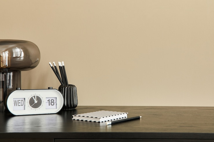 Foto stilvolle komposition der büroeinrichtung mit schwarzem schreibtisch, design-tischlampe, weißer uhr, notizbuch und schreibtisch-organizer. beige wand. platz kopieren.
