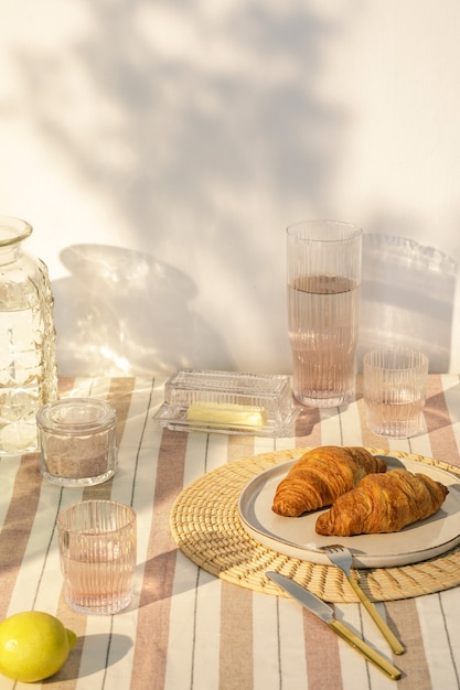 Stilvolle Komposition des Küchenbereichs im Freien mit Holztisch, Speisen, Getränken, Küchenzubehör, beiger Tischdecke und Sommerschatten von Bäumen. Landseitige Stimmung. Vorlage.