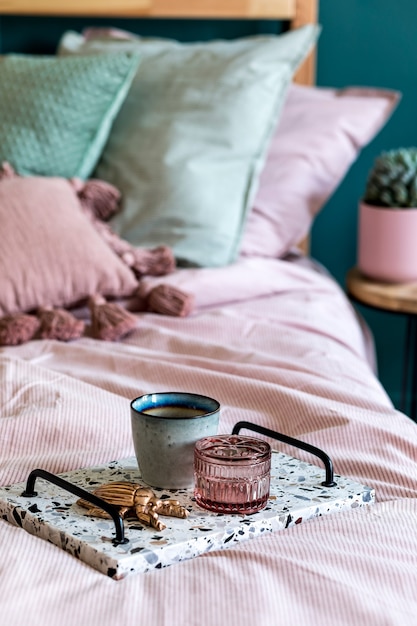 Stilvolle Komposition des Schlafzimmer-Interieurs mit Lastrico-Tablett mit Kaffee und eleganten persönlichen Accessoires. Schöne rosa und grüne Bettwäsche, Decke und Kissen. Design Home Staging. Nahansicht