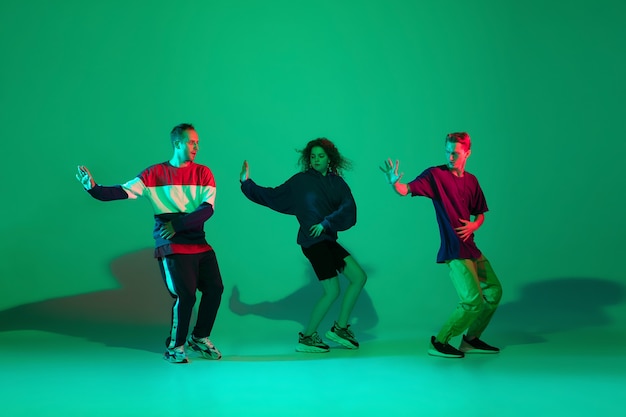Stilvolle Männer und Frauen tanzen Hip-Hop in hellen Kleidern auf grünem Hintergrund im Tanzsaal im Neonlicht. Jugendkultur, Bewegung, Stil und Mode, Action. Modisches Porträt.