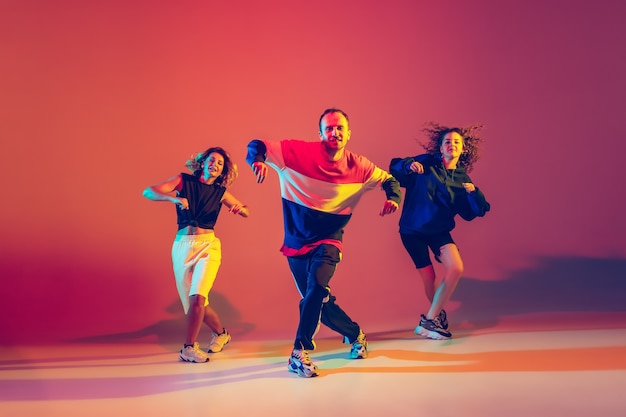 Stilvolle Männer und Frauen tanzen Hip-Hop in hellen Kleidern auf Hintergrund mit Farbverlauf