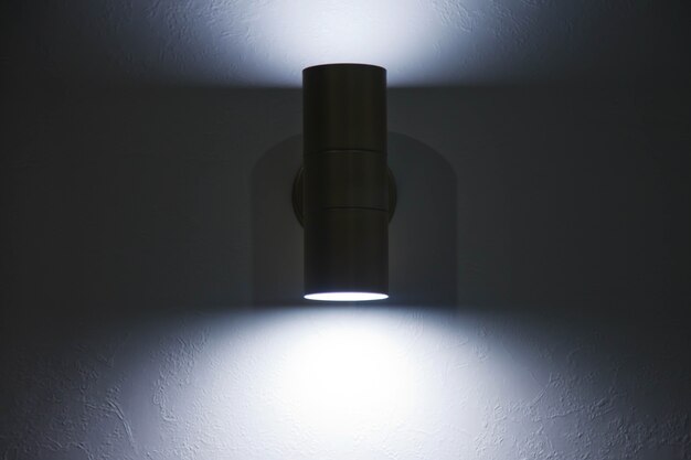 Stilvolle moderne Lampe auf weißer strukturierter Wand. Glühende Chrom-LED-Lampe an grauer Wand. Freier Platz und dunklerer Streifen auf dem Hintergrund für Inschrift. Copyright-Bereich für Website oder Banner