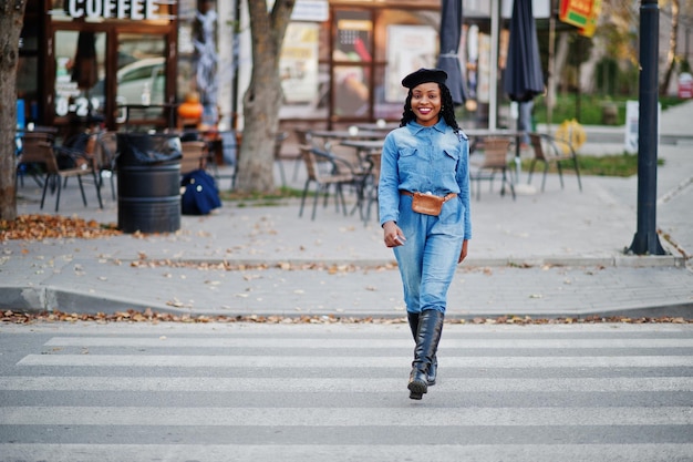Stilvolle, modische afroamerikanische Frauen in Jeans und schwarzer Baskenmütze, die auf dem Fußgängerverkehr laufen