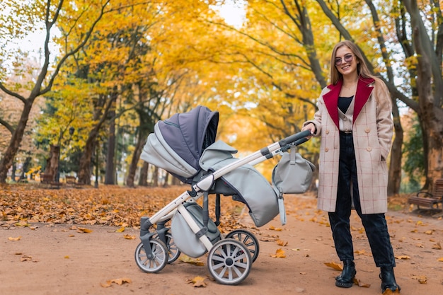 Stilvolle Mutter mit Kinderwagen im Herbstpark