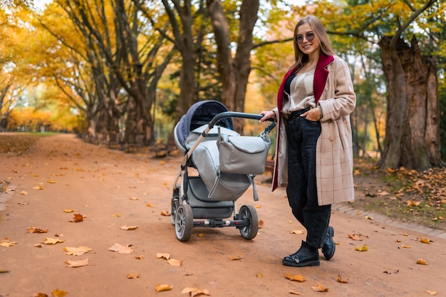 Stilvolle Mutter mit Kinderwagen im Herbstpark