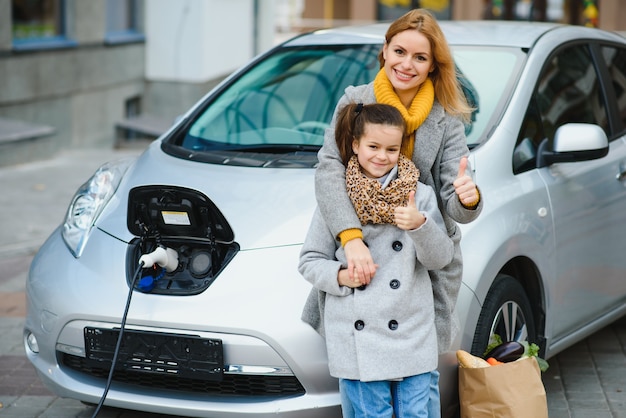 Stilvolle Mutter und Tochter laden ein Elektroauto auf und verbringen Zeit miteinander