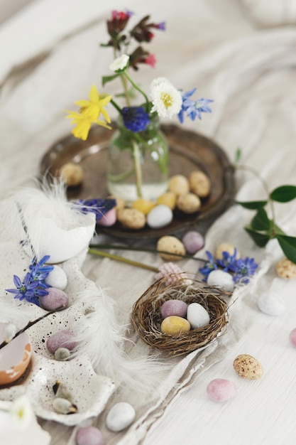 Stilvolle Oster-Schokolade-Eier im Nest Frühlingsblumen Federn und Leinentuch auf rustikaler