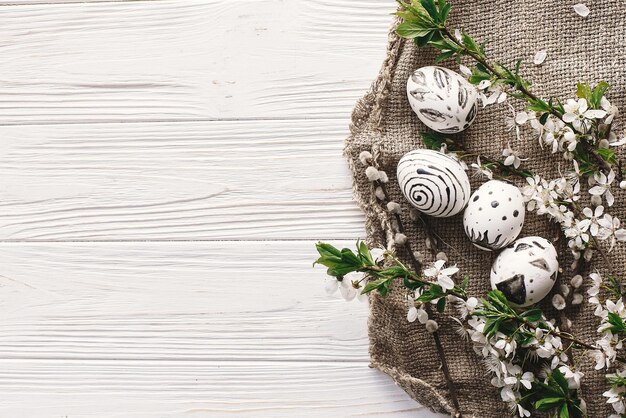 Stilvolle Osterwohnung lag mit bemalten Eiern in Schwarz-Weiß-Farben auf rustikalem Holzhintergrund mit Frühlingsblumen Frohe Ostern Grußkarte Platz für Text Moderne Ostereier