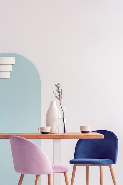 Stilvolle pastellrosa und petrolblaue Stühle am langen Holztisch im hellen Esszimmer