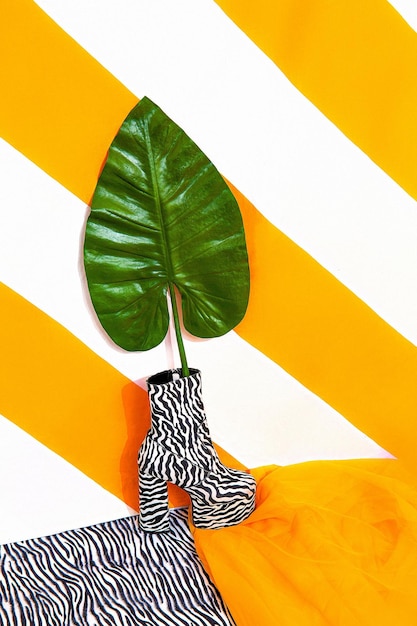 Stilvolle Plateau-Damenstiefel auf hellgelb gestreiftem Hintergrund. Tropisches exotisches Minimalkonzept. Gelb und Zebradruck gemischt. Stilleben-Modetrends