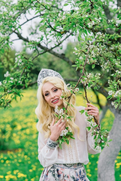 Stilvolle russische Frau in traditioneller nationaler Volkstracht, slawischer Kopfschmuck, weiße Frühlingsblumen.