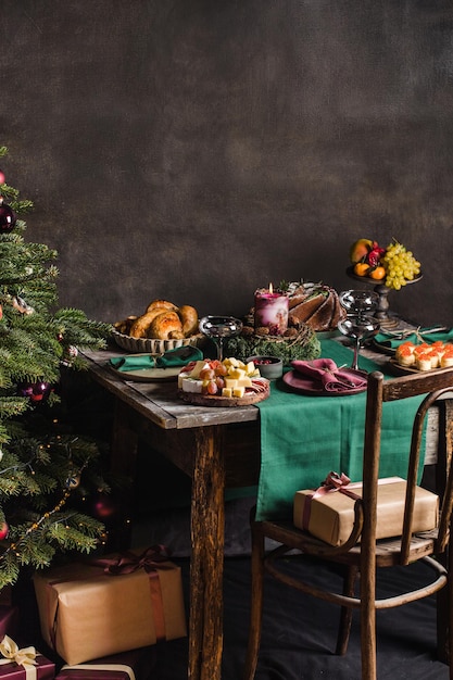 Stilvolle Tischdekoration für Weihnachtsessen mit der Familie mit Weihnachtsbaum im Hintergrund und Geschenken auf...
