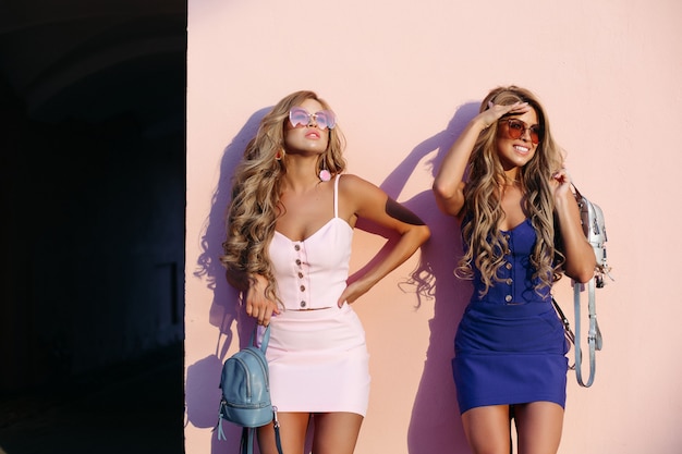 Stilvolle und schicke Frauen, die in der Sonnenbrille und mit blauen Geldbörsen aufwerfen