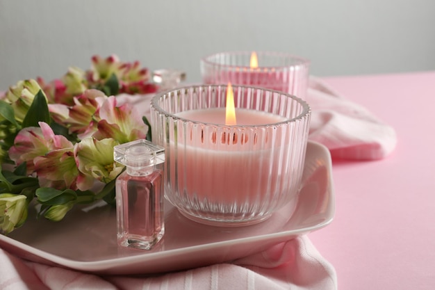 Stilvolle zarte Komposition mit brennenden Kerzen und Blumen auf rosafarbenem Tisch Gemütliches Innenelement