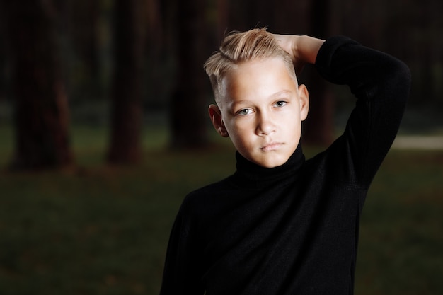 Foto stilvoller attraktiver junger mann mit einer modischen frisur in einem trendigen schwarzen outfit genießt einen urlaub im freien im park.