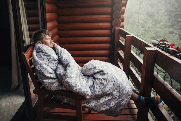 Foto stilvoller bärtiger mann, der sich auf einer hölzernen veranda inmitten von wäldern in regnerischen bergen entspannt
