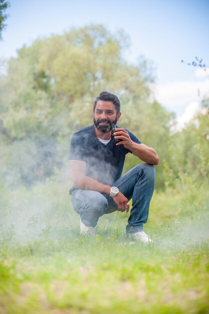 Stilvoller bärtiger Mann mit elektronischer Zigarette auf dem Gras. Konzept der elektronischen Zigarette.