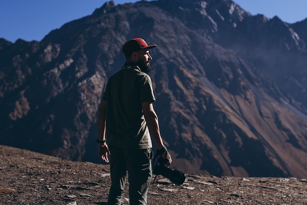 Stilvoller bärtiger Mann mit Kamera in der Hand auf der Spitze des Naturfotografen der georgischen Berge