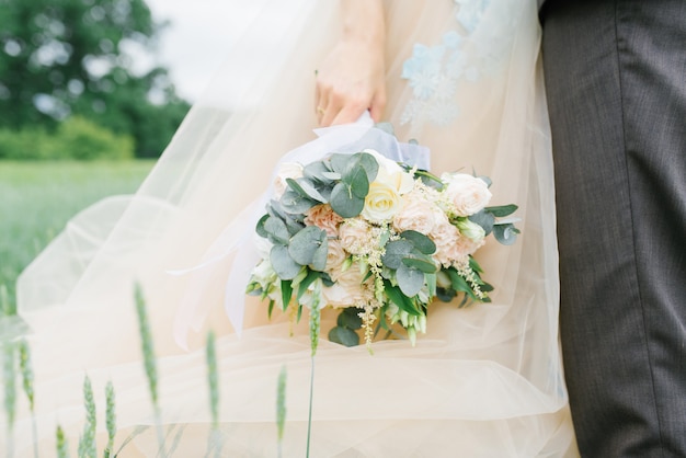 Stilvoller empfindlicher Hochzeitsblumenstrauß in den Händen der Braut auf dem Hintergrund des Hochzeitskleides