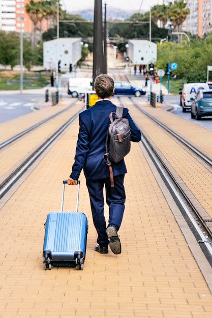 Stilvoller Geschäftsmann im Anzug mit Koffer läuft vom Zug aus die Gleise entlang