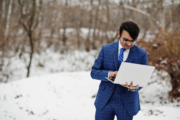 Stilvoller indischer Geschäftsmann in Anzug und Brille posierte am Wintertag im Freien mit Laptop in der Hand