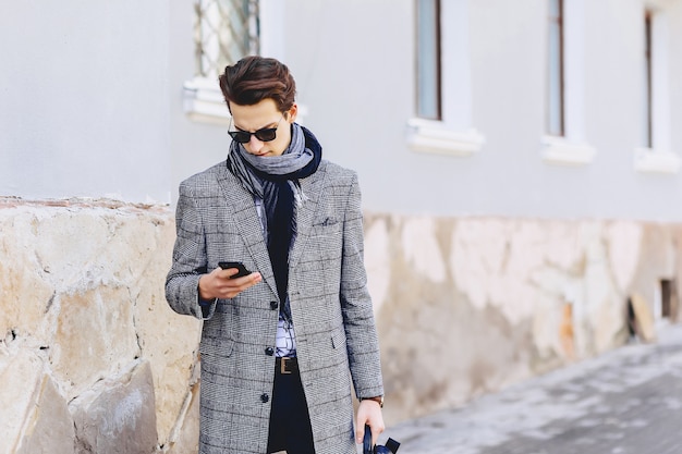 Stilvoller junger Mann in der Sonnenbrille mit Telefon auf Straße