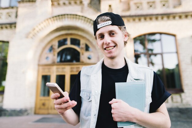 Stilvoller junger Student, der eine Kappe nahe der Universität trägt