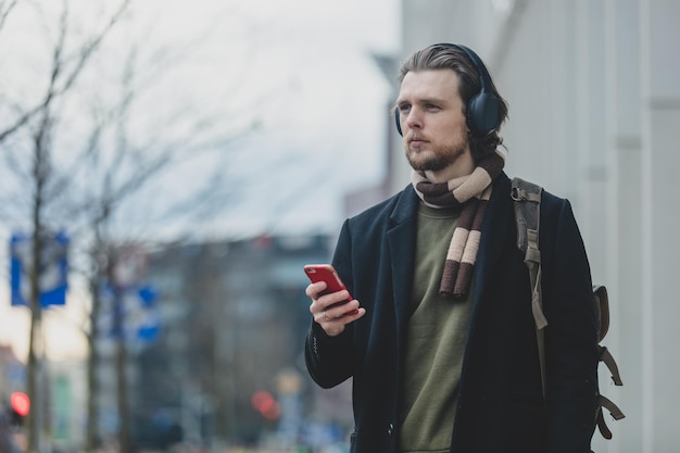 Stilvoller Kerl in Schal und Mantel hören Sie Musik im Streaming-Dienst mit dem Handy auf der Straße von Wroclaw Polen