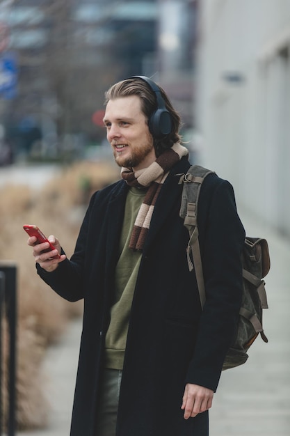 Stilvoller Kerl in Schal und Mantel hören Sie Musik im Streaming-Dienst mit dem Handy auf der Straße von Wroclaw Polen