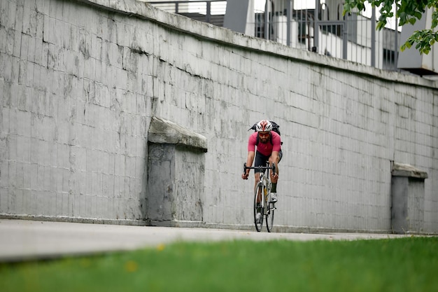 Stilvoller Mann, der an einem Wochenende mit dem Fahrrad durch die Stadt läuft und auf dem Hintergrund einer grauen Wand reitet Minimalistisches Foto eines Radfahrers auf dem Hintergrund einer grauen Wand