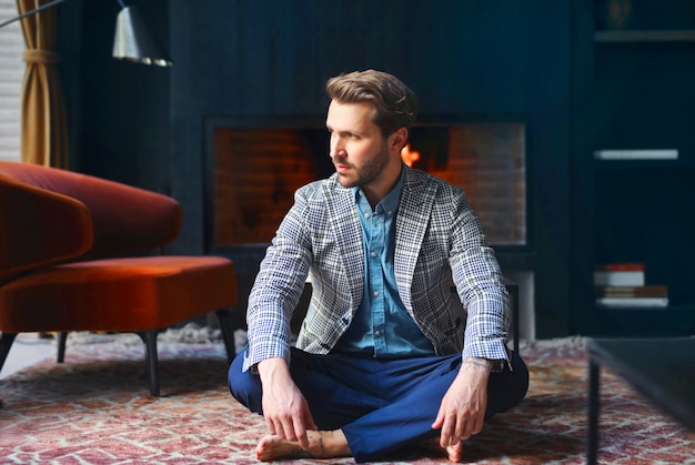 Stilvoller Mann, der auf einem Teppich sitzt