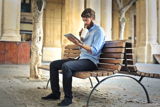 Stilvoller Mann, der auf einer Bank sitzt und eine Tablette verwendet