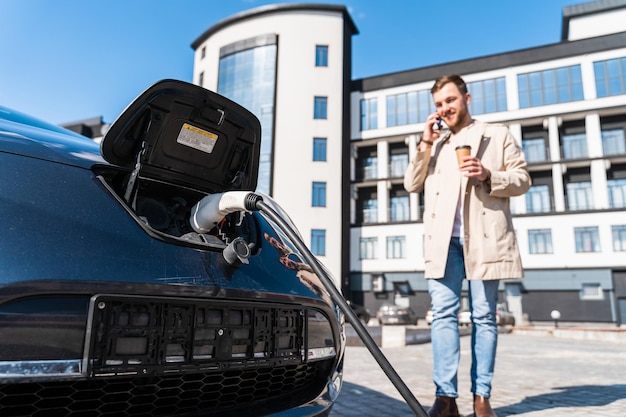 Stilvoller Mann, der wartet, während sein Auto an der Station aufgeladen wird