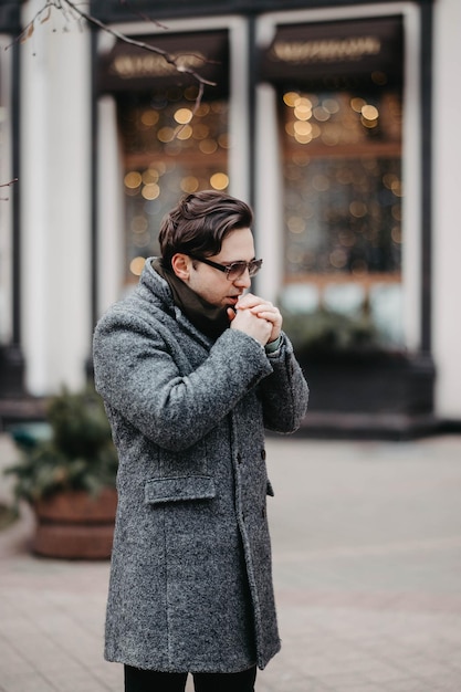 Stilvoller Mann in grauem Mantel und Sonnenbrille, der in der Stadt spazieren geht.