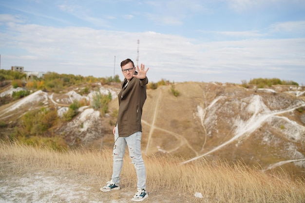 Stilvoller Mann mit Brille im Umhang zeigt psychisch Erwachsener Mann mit Brille posiert in hügeligem Gelände