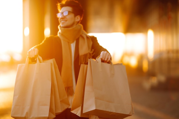 Stilvoller Mann mit Papierpaketen nach dem Einkaufen bei Sonnenuntergang Schöner Mann beim Einkaufen