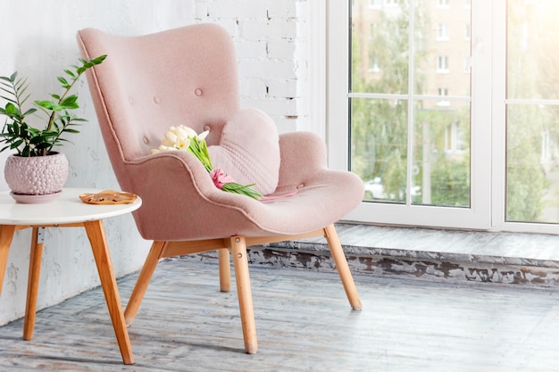 Stilvoller rosa Sessel mit herzförmigem Kissen in einem hellen minimalistischen Innenraum