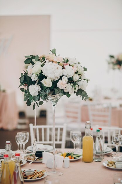 Stilvoller rosafarbener Hochzeitstisch mit Gläsern, Besteck, Serviette und köstlichen Speisen und Getränken mit großem Blumenstrauß im Zentrum, Luxus-Catering im Restaurant, Hochzeitsempfang