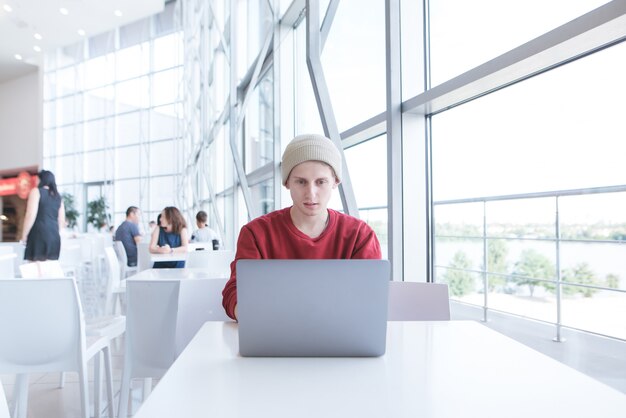 Stilvoller Student in der Freizeitkleidung, die in einem hellen Café sitzt und einen Laptop benutzt