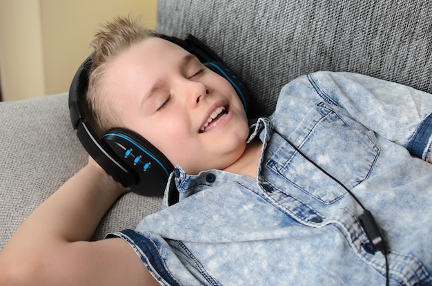Stilvoller Teenager, der Musik in Kopfhörern hört und zu Hause singt, glücklicher lächelnder Junge, der zu Hause auf dem Sofa ruht
