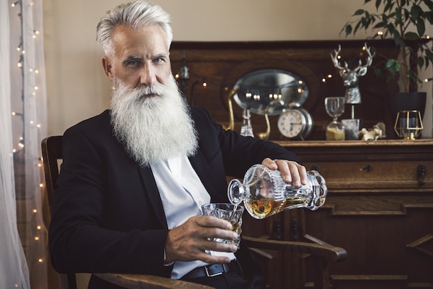 Stilvoller und gutaussehender bärtiger älterer Mann, der Whisky in das Glas gießt